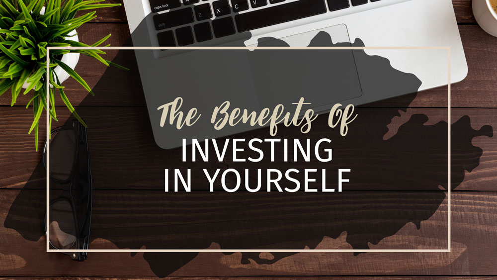 Text: The Benefits of Investing in Yourself Beckground: Black overlay on woood desk with plant, keyboard and glasses